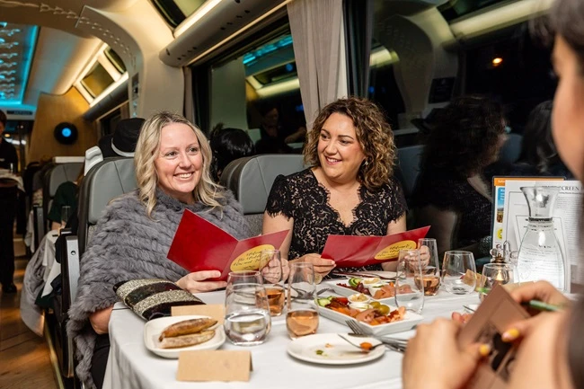 Two women on the Tormore Express event train read clue booklets and enjoy a meal