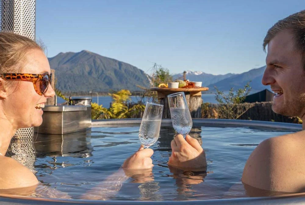 Couple soaking in the Hotel Lake Brunner Wood Fired Hot Tub with wine