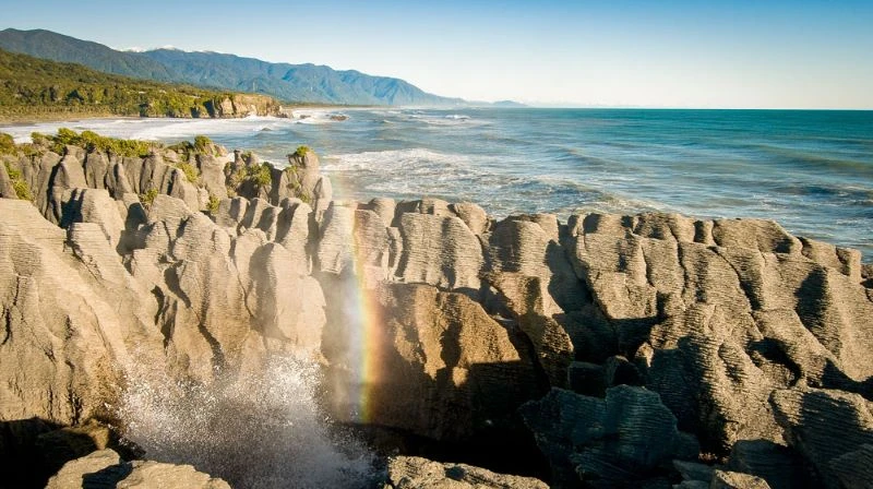 Punakaiki Pancake Rocks with ocean in the background and a rainbow in the foreground