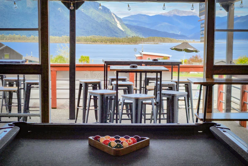 View out of Hotel Lake Brunner, including a pool table, outdoor seating, and beautiful views