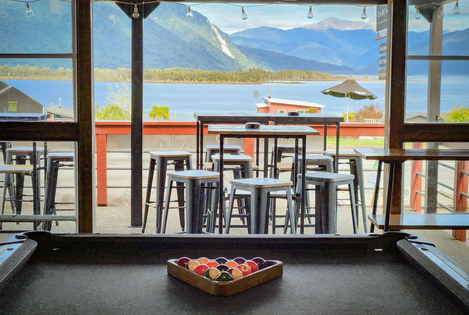 View out of Hotel Lake Brunner, including a pool table, outdoor seating, and beautiful views