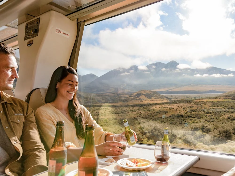 Couple enjoying a drink aboard the TranzAlpine passing Mount Binser
