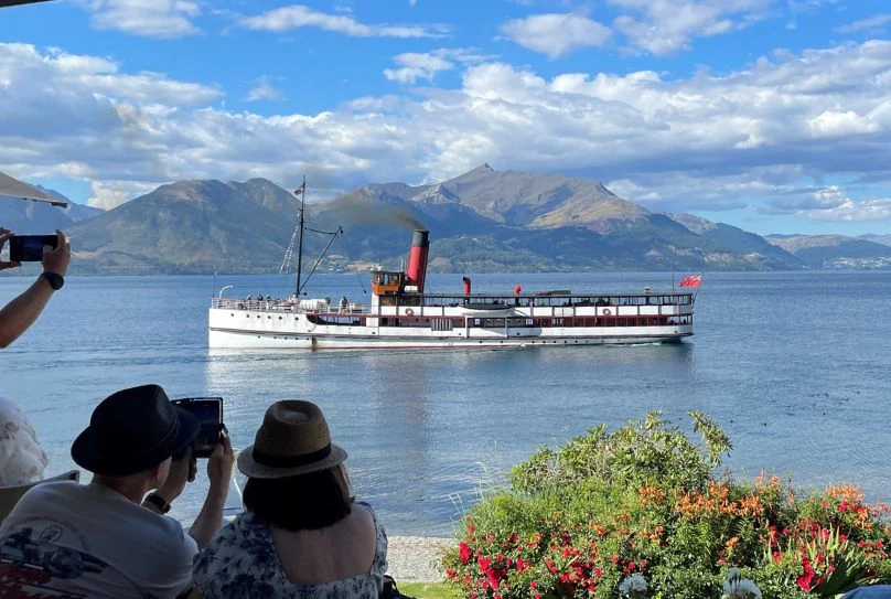 Woman on the shore in Queenstown photographing the TSS Earnslaw ship in the bay