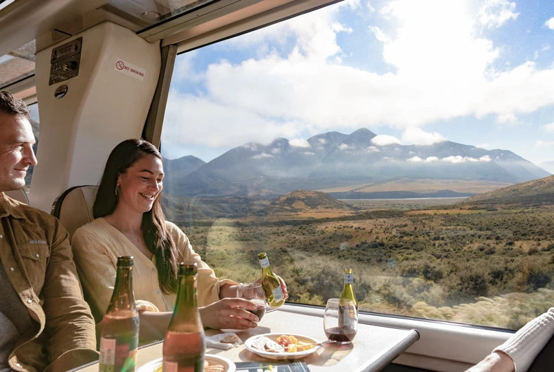 Couple enjoying a drink aboard the TranzAlpine passing Mount Binser